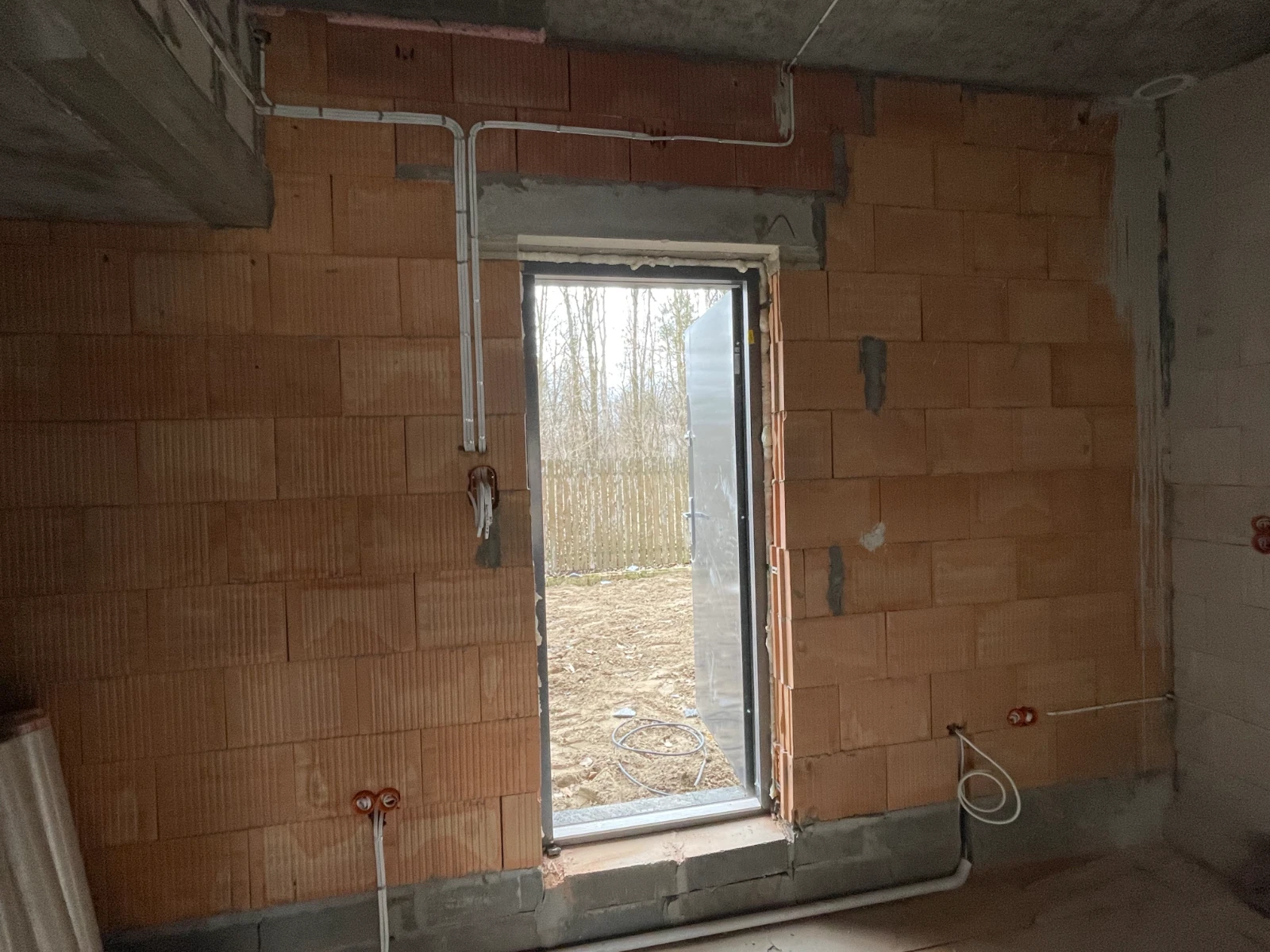 Instalacje elektryczne w surowym wnętrzu: przewody i puszki zamontowane przy ceglanej ścianie i otworze drzwiowym